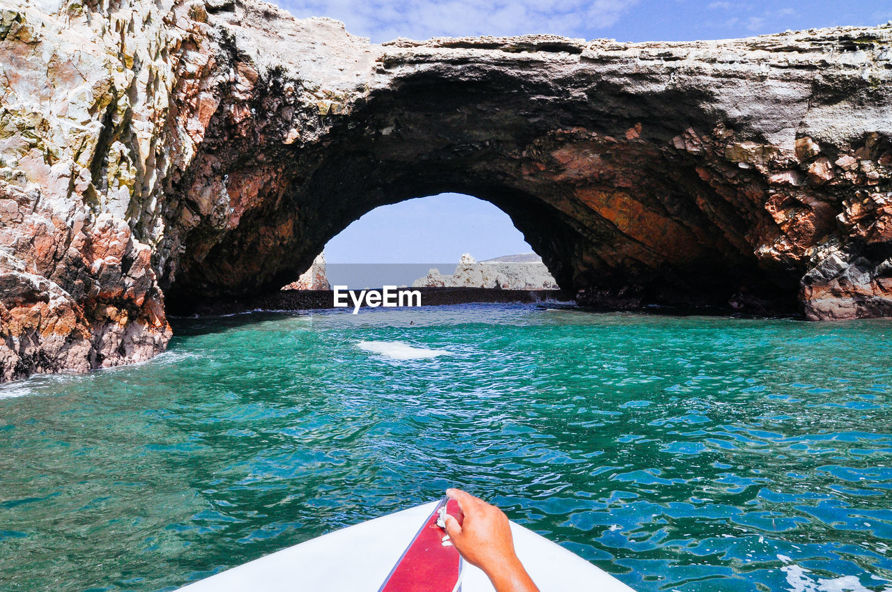 Cropped hand holding in boat on sea against rock formation