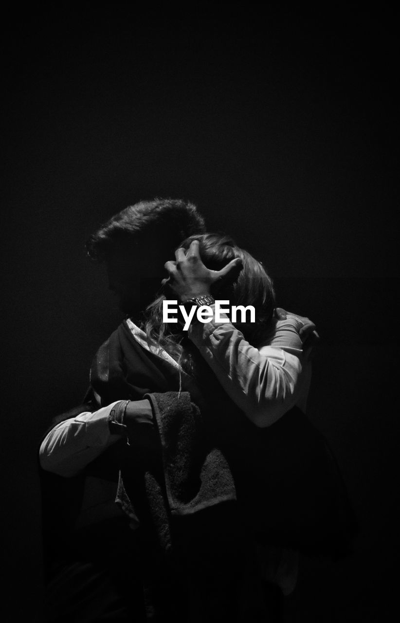 Couple embracing against black background