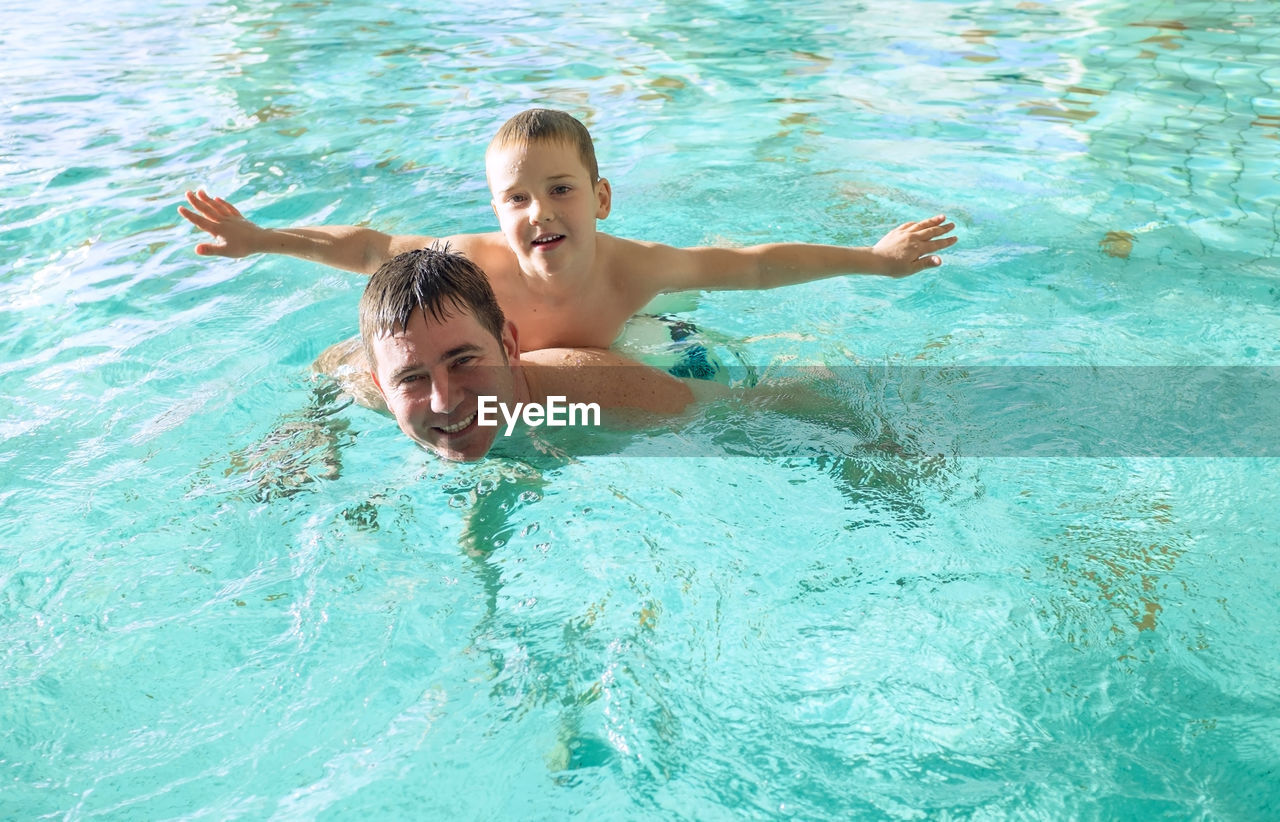 Happy father and son swimming lesson in pool. child learning swim. family, parenthood, health, sport