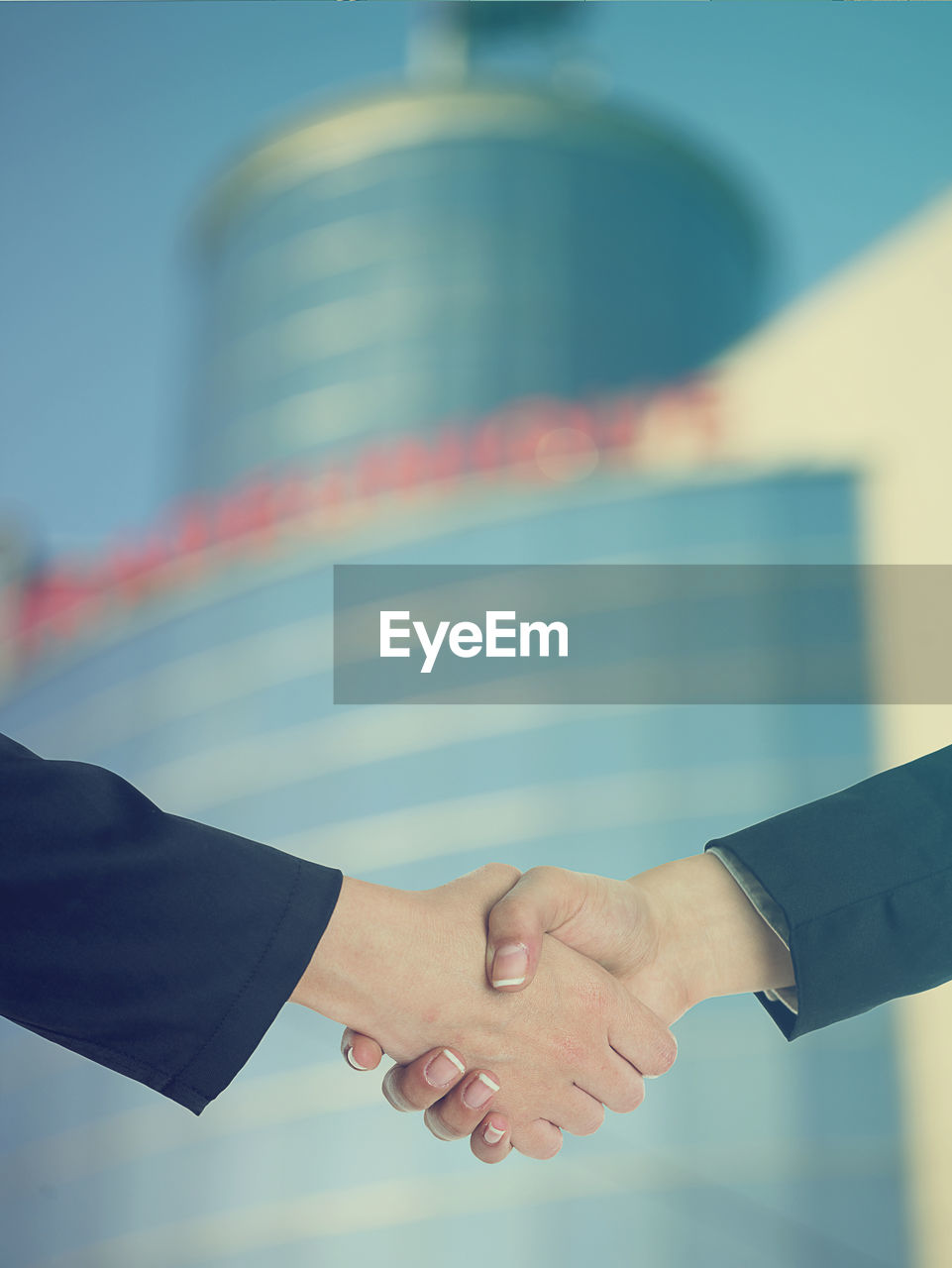 Cropped image of businesswomen shaking hands against building