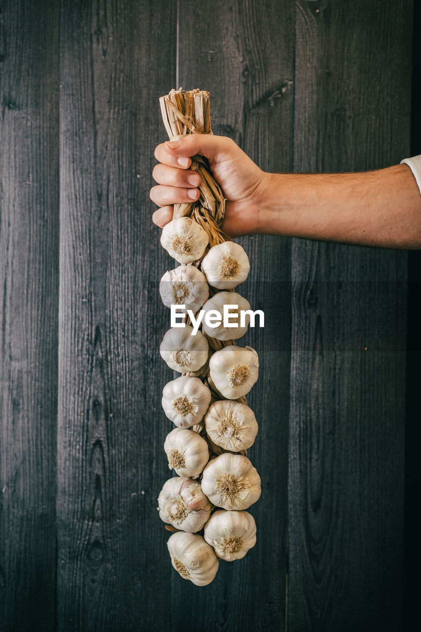 Unrecognizable person holding and showing a bunch of healthy fresh garlic against black lumber wall person