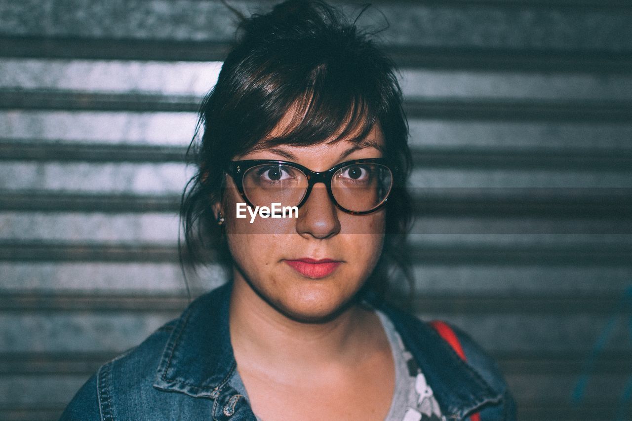 Portrait of woman wearing eyeglasses against corrugated iron