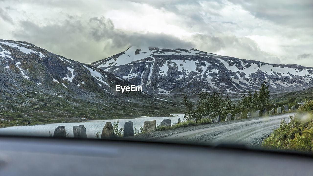 Road by snowcapped mountains against sky seen through car windshield