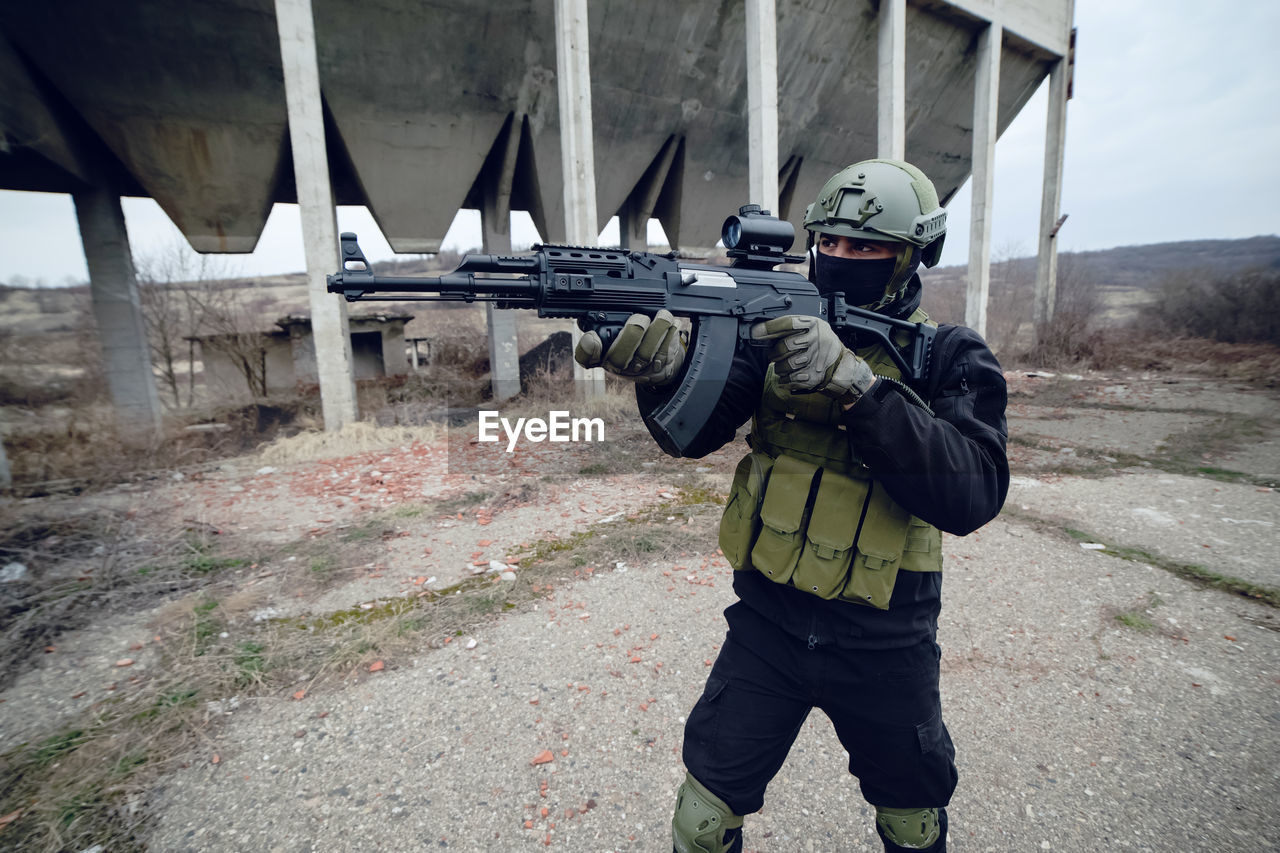 Army soldier aiming while standing against built structure