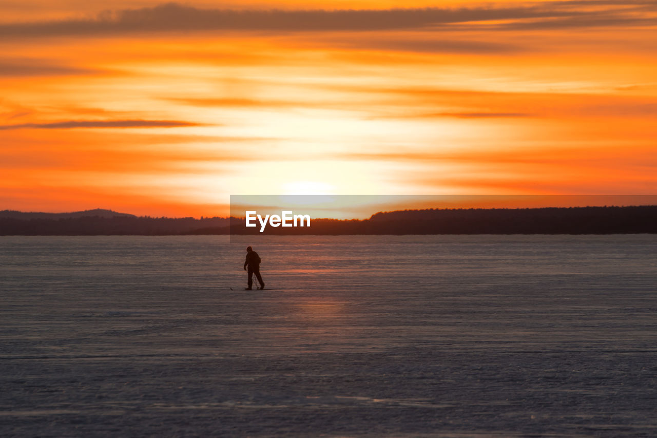 SILHOUETTE MAN IN SEA AGAINST ORANGE SKY