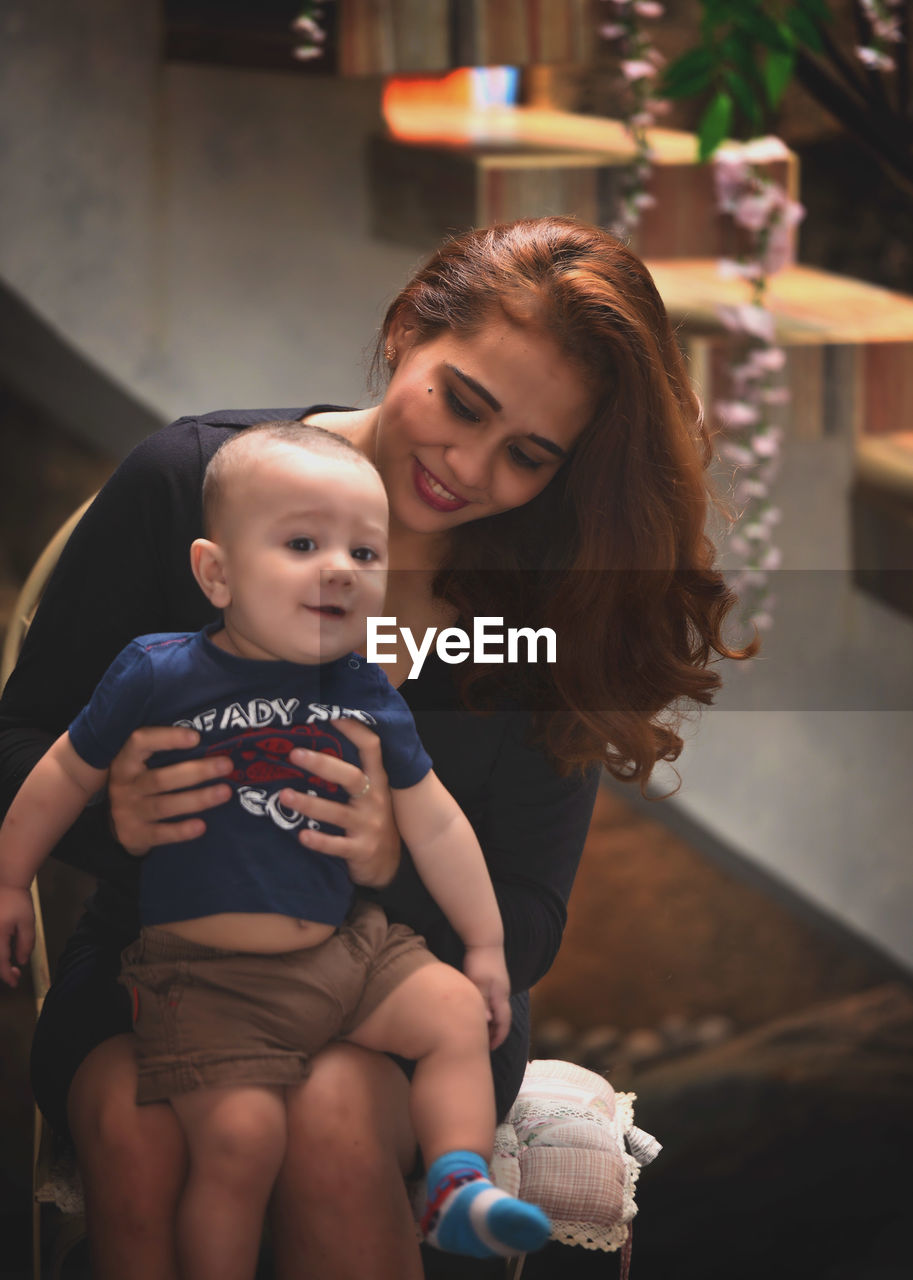 Portrait of son with mother sitting on chair at home