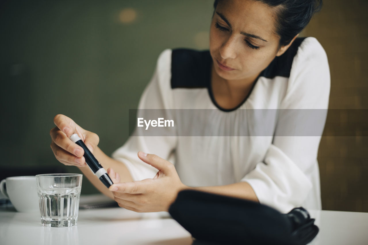 Businesswoman checking blood sugar level with diabetes kit at table