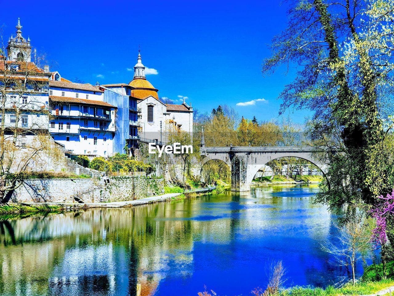 Bridge over river by buildings against blue sky