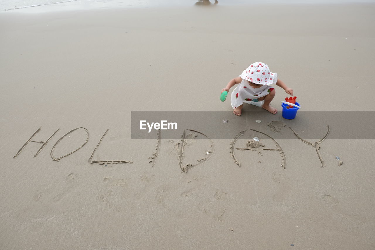 High angle view of girl crouching by text on sand at beach