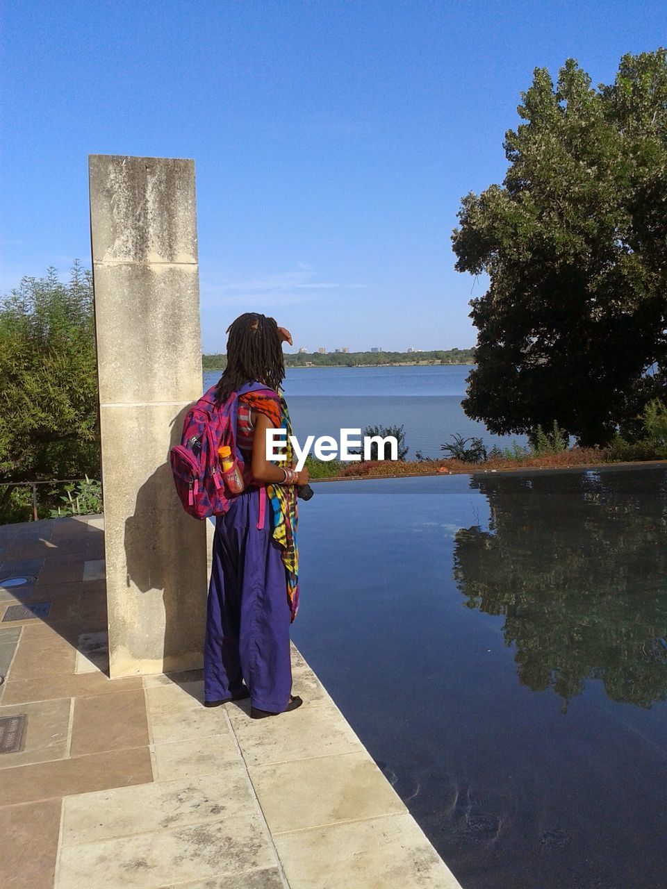 Side view of young woman standing on lakeshore against clear sky