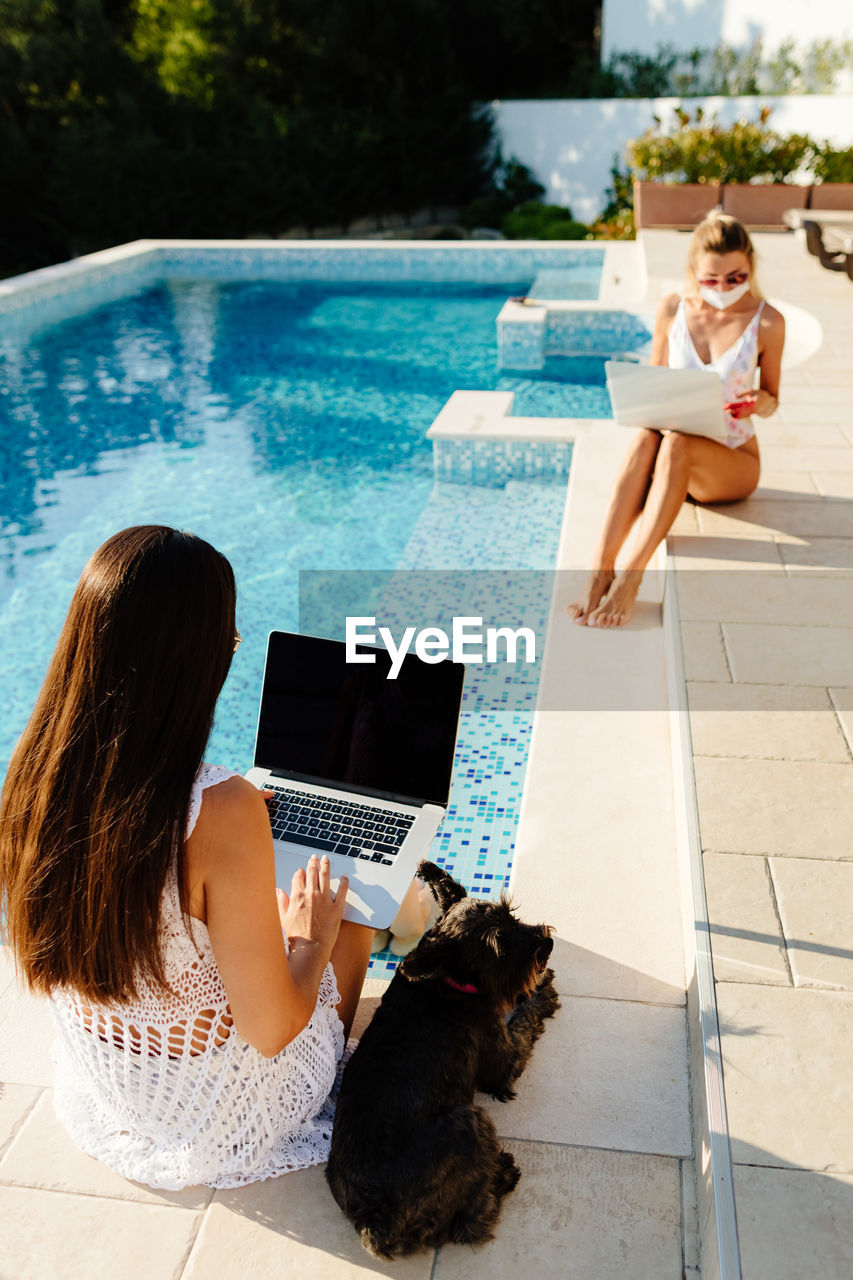 Women using laptop sitting by pool