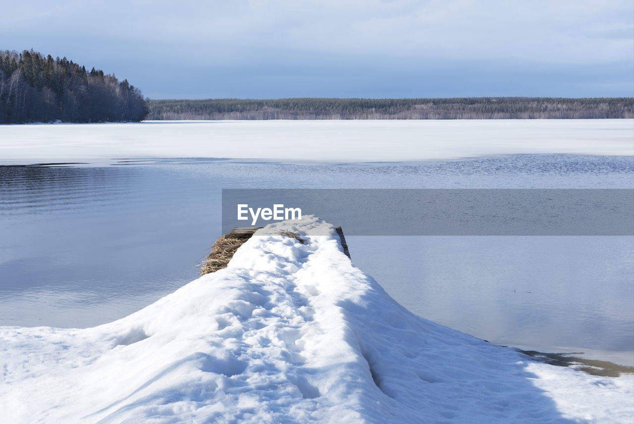 A pier in the snow on the lake. melting of ice on the lake in early spring. calm serenity nature.