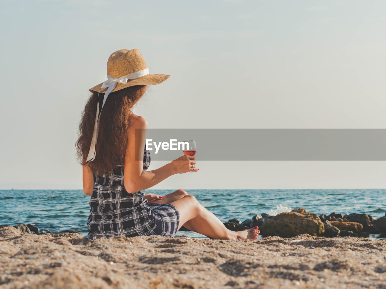 Woman having wine while sitting at beach against sky