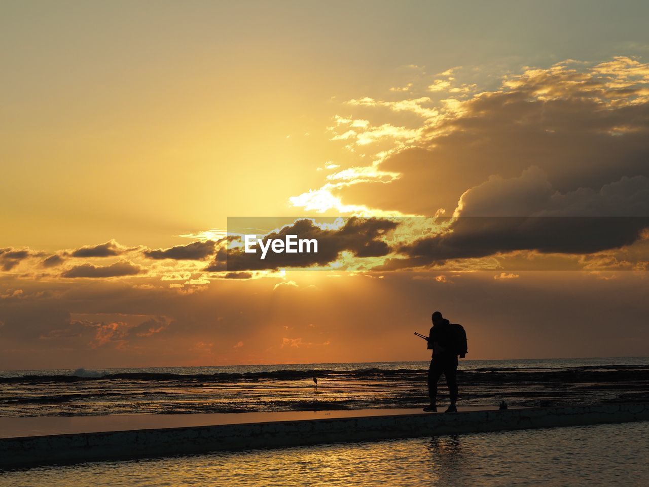 Silhouette man standing on beach against sky during sunset