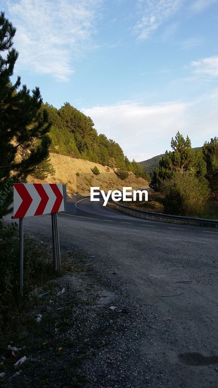 Sign board on street by mountain against sky