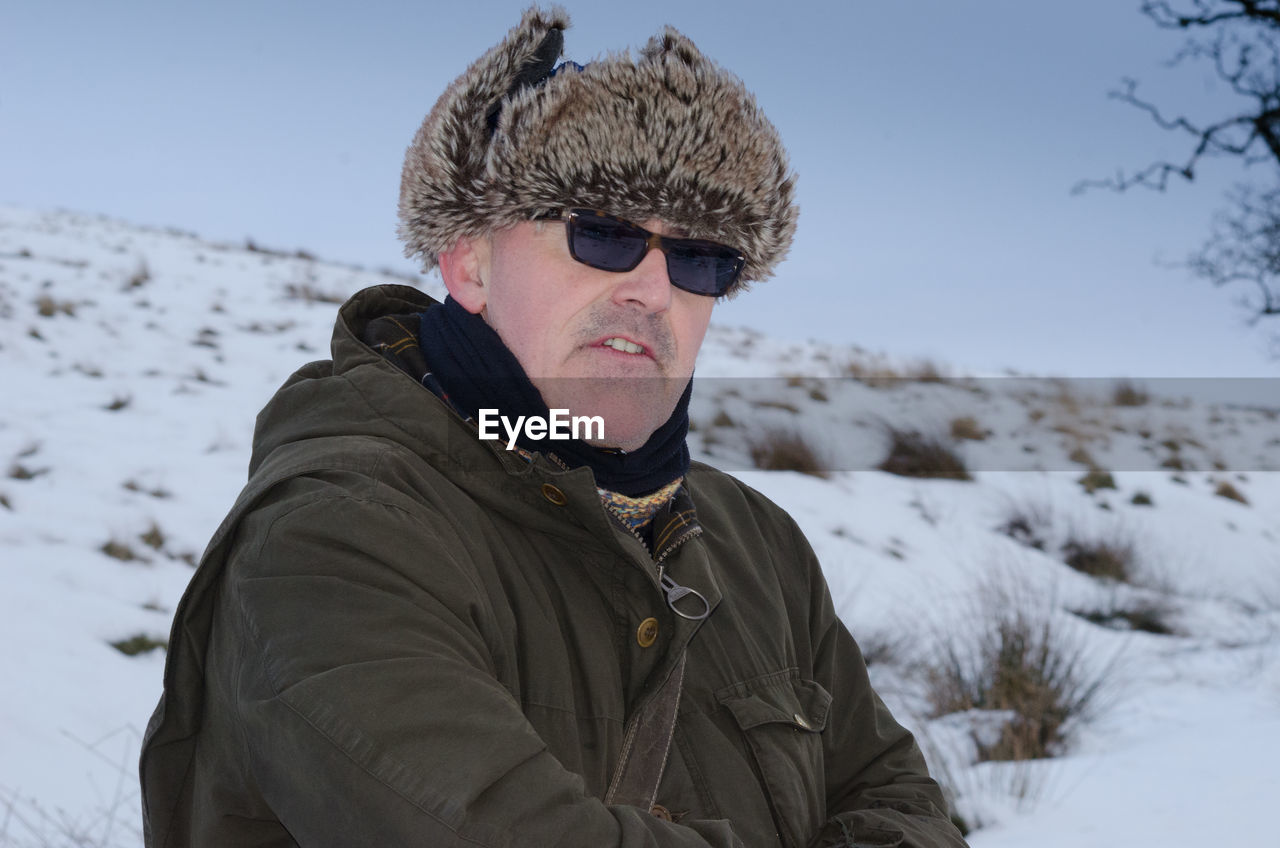 Man wearing fur deerstalker hat while standing on snowy field