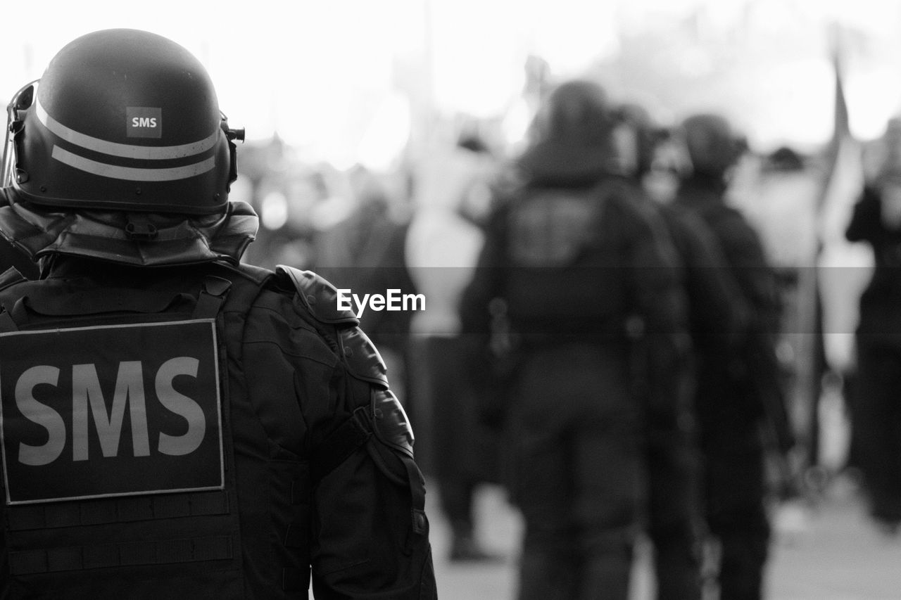 government, uniform, security, police force, black and white, protection, law, clothing, police, monochrome, helmet, person, armed forces, adult, rear view, men, military, headwear, violence, monochrome photography, group of people, police officer, work helmet, emergency services occupation, accidents and disasters, authority, focus on foreground, black, military uniform, occupation, soldier, day, standing, army