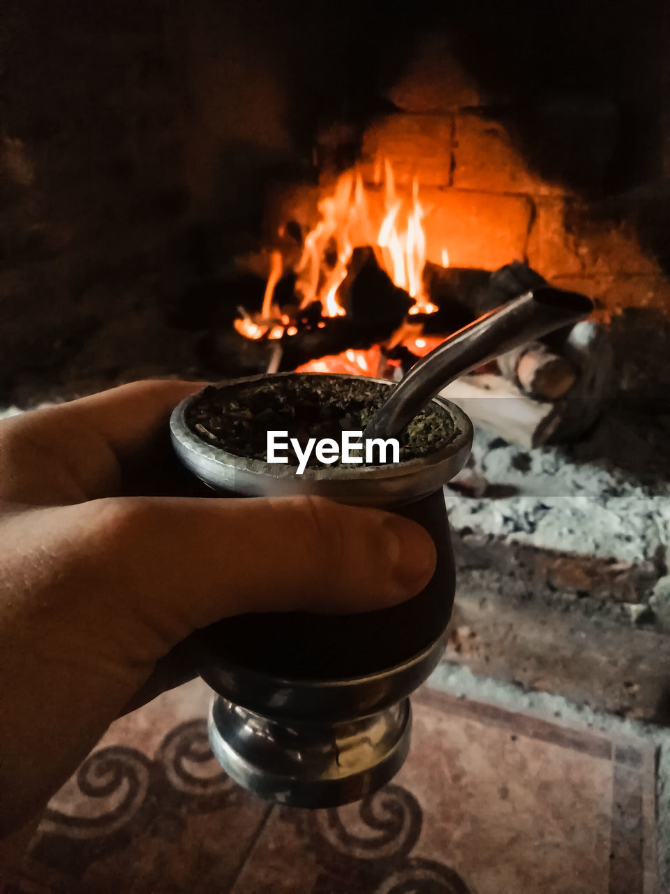 Close-up of hand holding container against fireplace