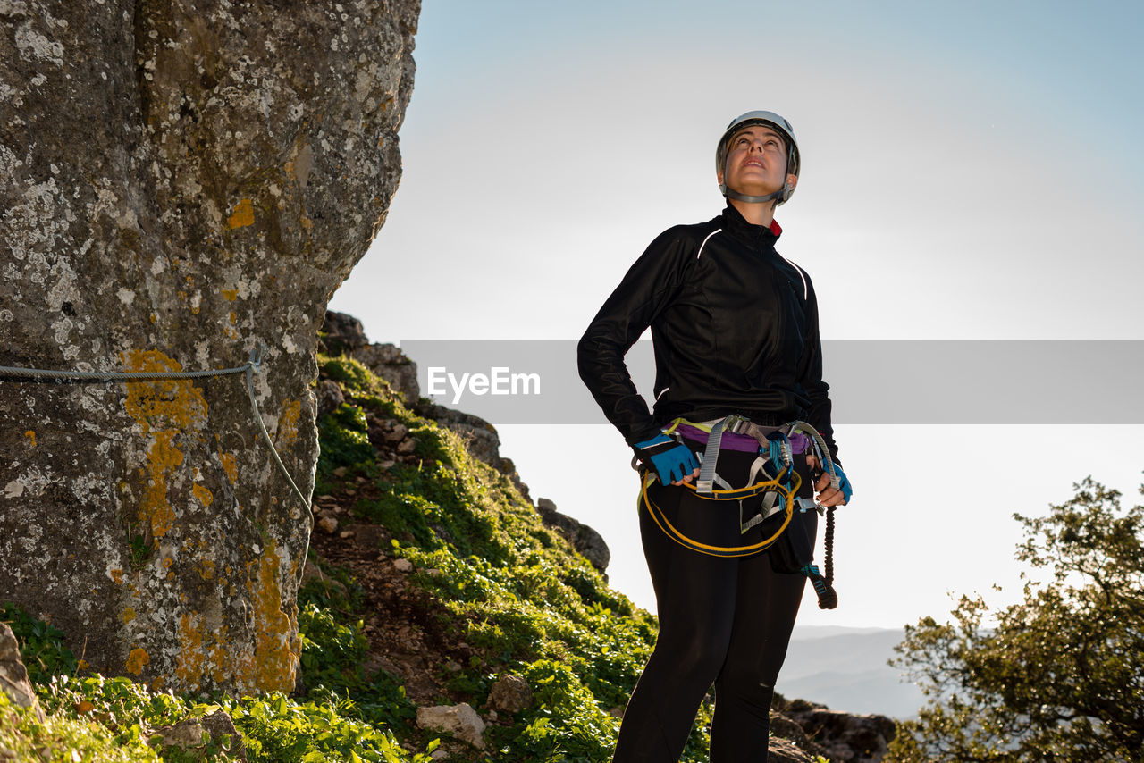 Concept: adventure. climber woman with helmet and harness. pensive standing on a rock. looking at the top of the mountain. solar luminous flare. via ferrata in the mountains.