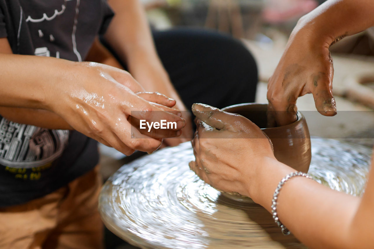 Midsection of people working on pottery wheel