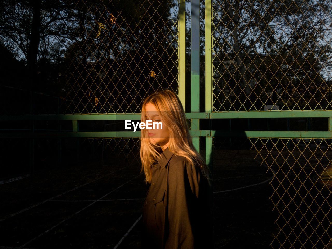 Woman standing by fence against trees