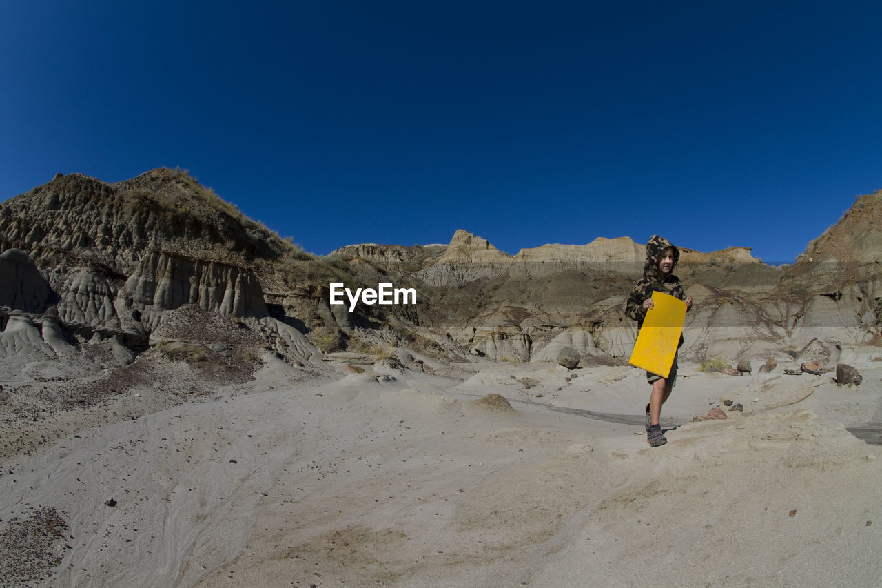 Boy walking on rock against clear blue sky