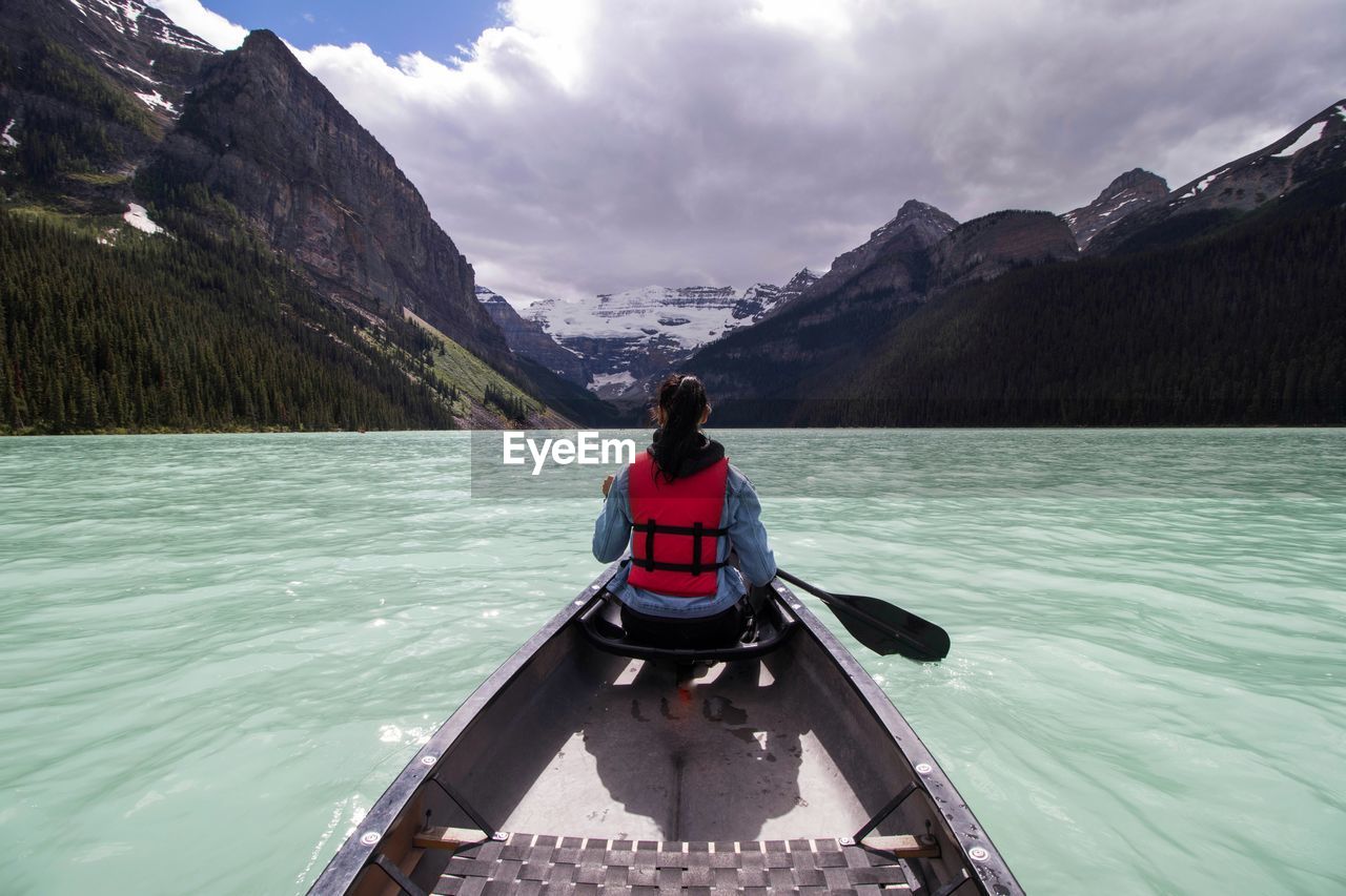 Rear view of woman rowing rowboat in lake towards mountains