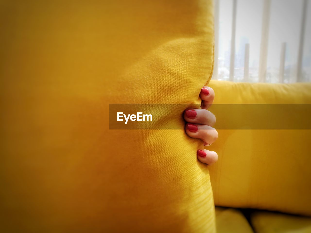 Cropped hand of woman holding yellow pillow