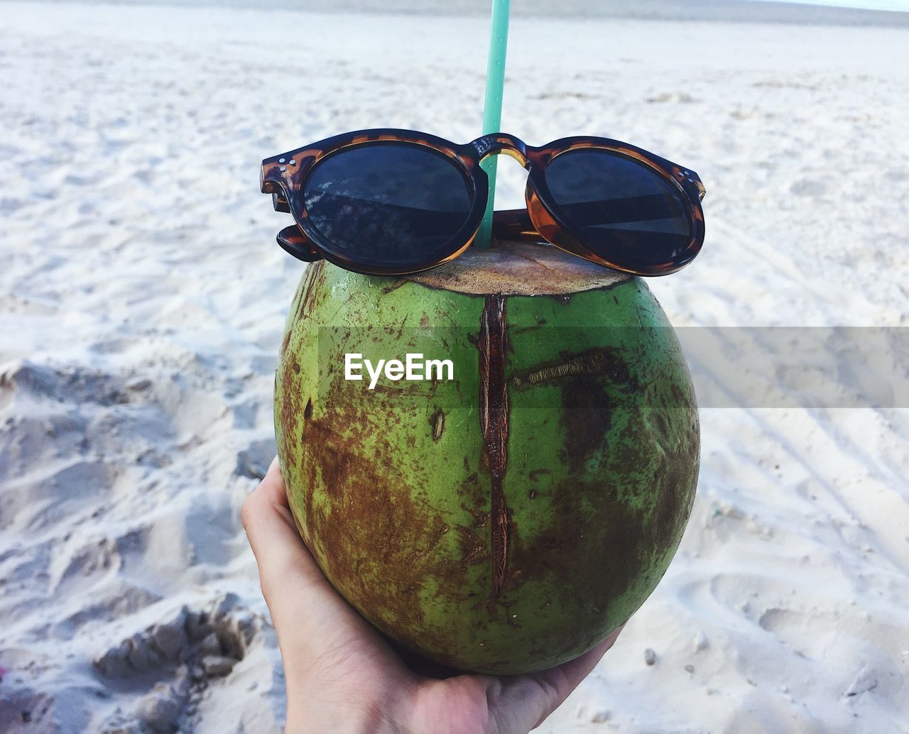 CLOSE-UP OF PERSON HAND HOLDING SUNGLASSES ON BEACH