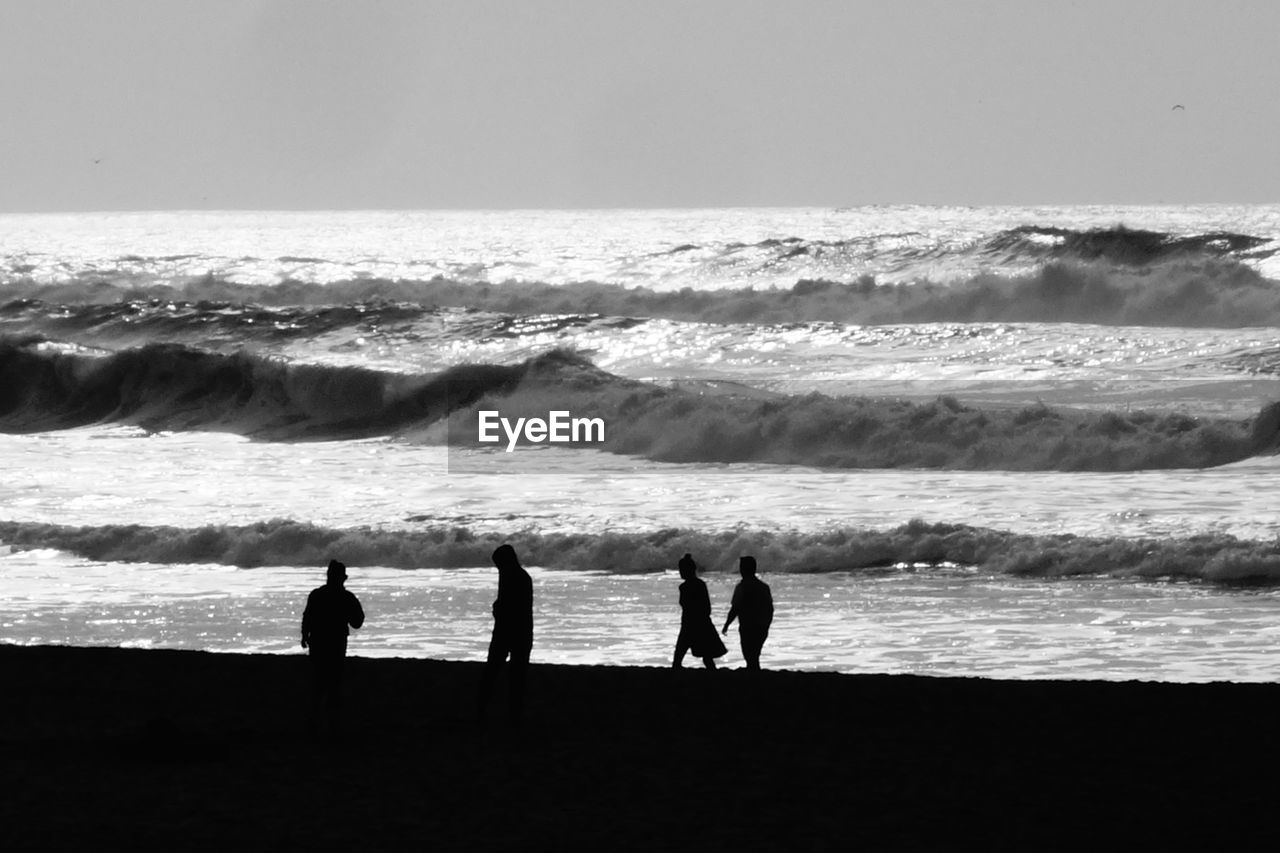 Silhouette people walking at beach against sky