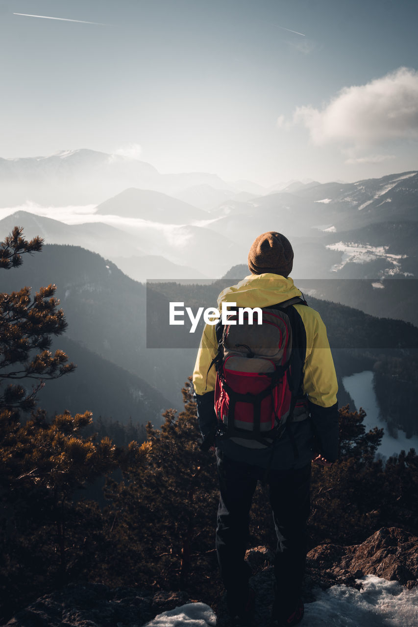 Rear view of man standing on mountain against sky