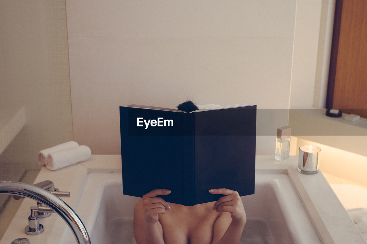 Midsection of woman reading book in bathtub