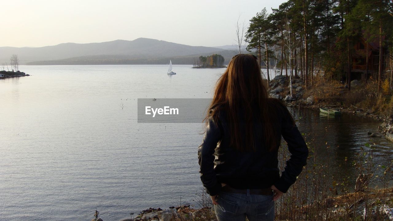Rear view of woman standing at shore of lake turgoyak