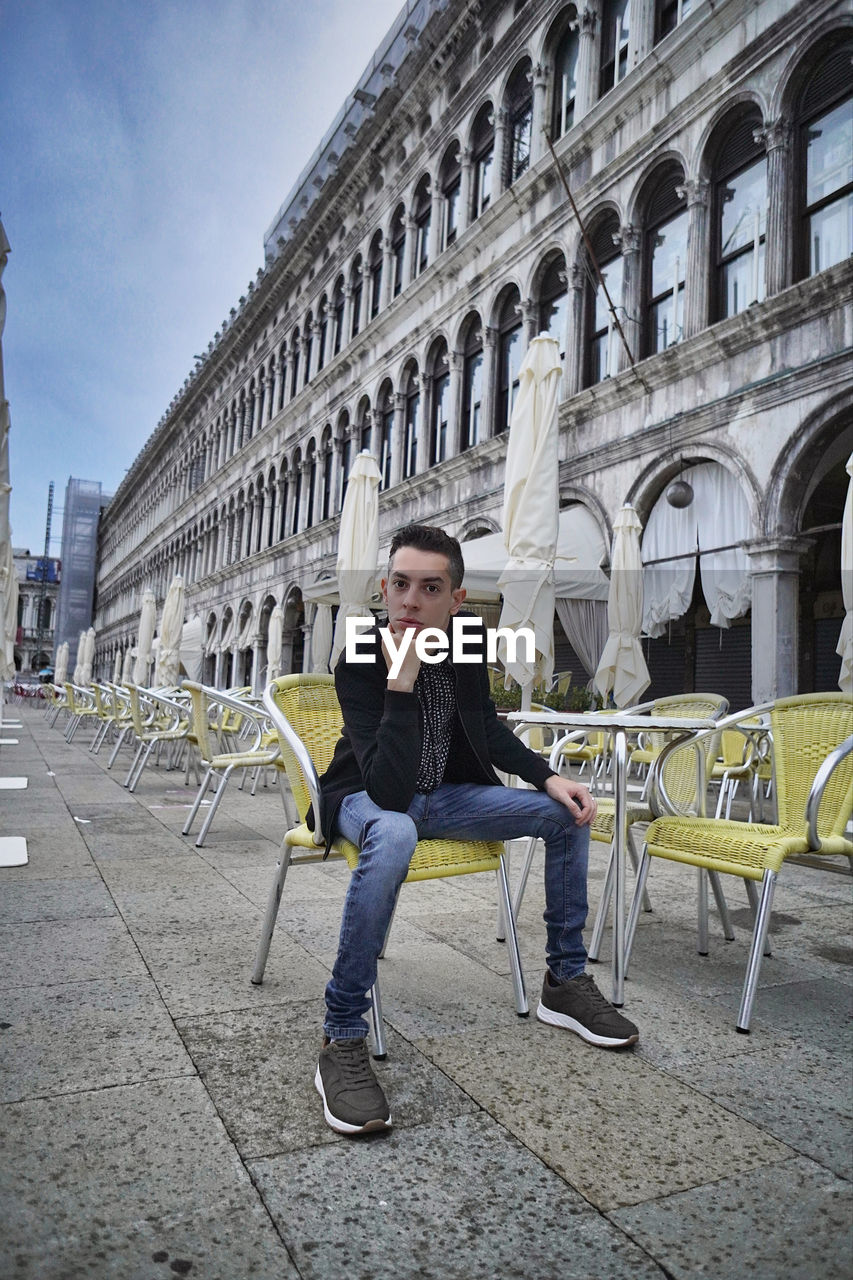 Full length of young man sitting on seat in city