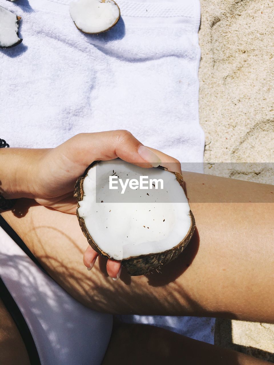 Midsection of woman holding coconut shell at beach during sunny day