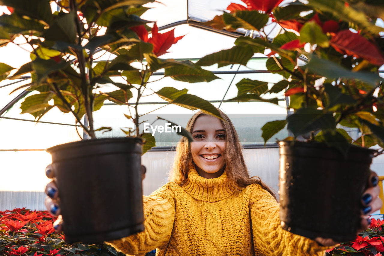 Portrait of smiling young woman holding flower plants