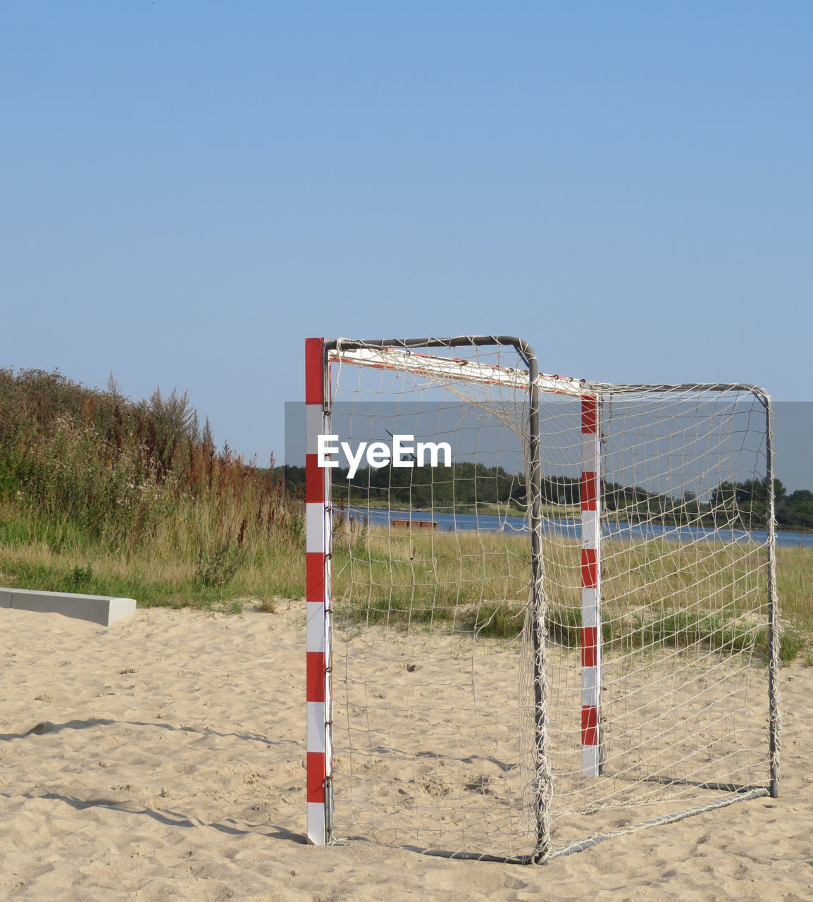 Soccer goal on sand against clear blue sky