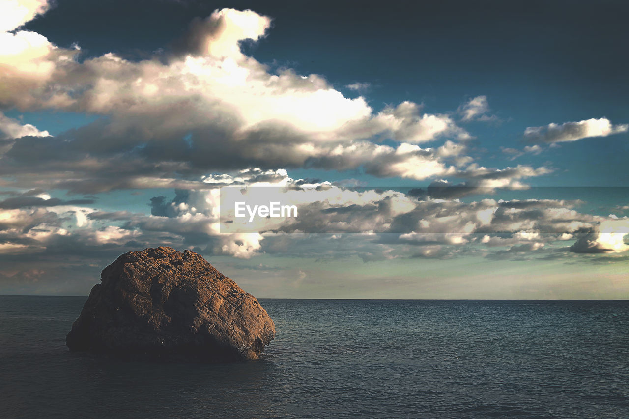 Rock at sea against cloudy sky