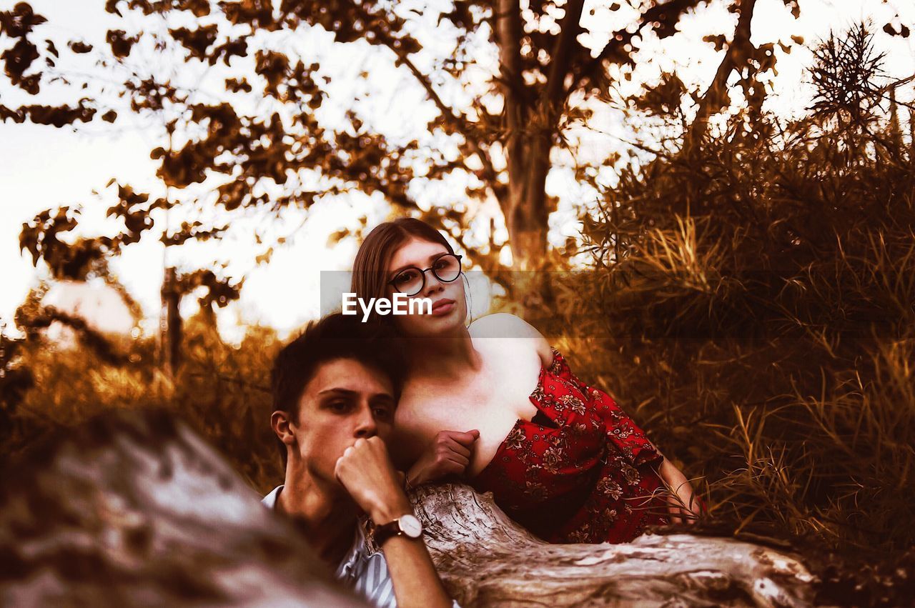 Portrait of couple leaning against tree trunk