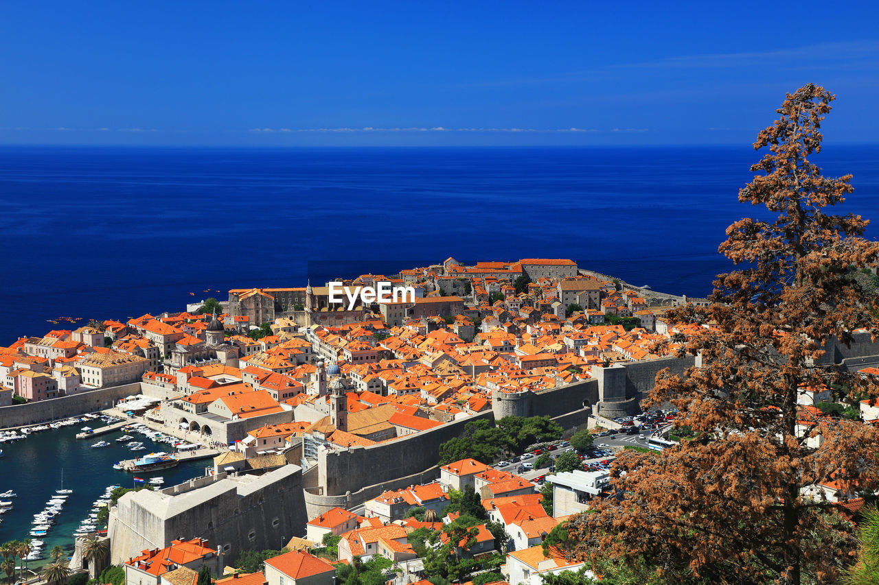 High angle view of cityscape by sea against clear blue sky