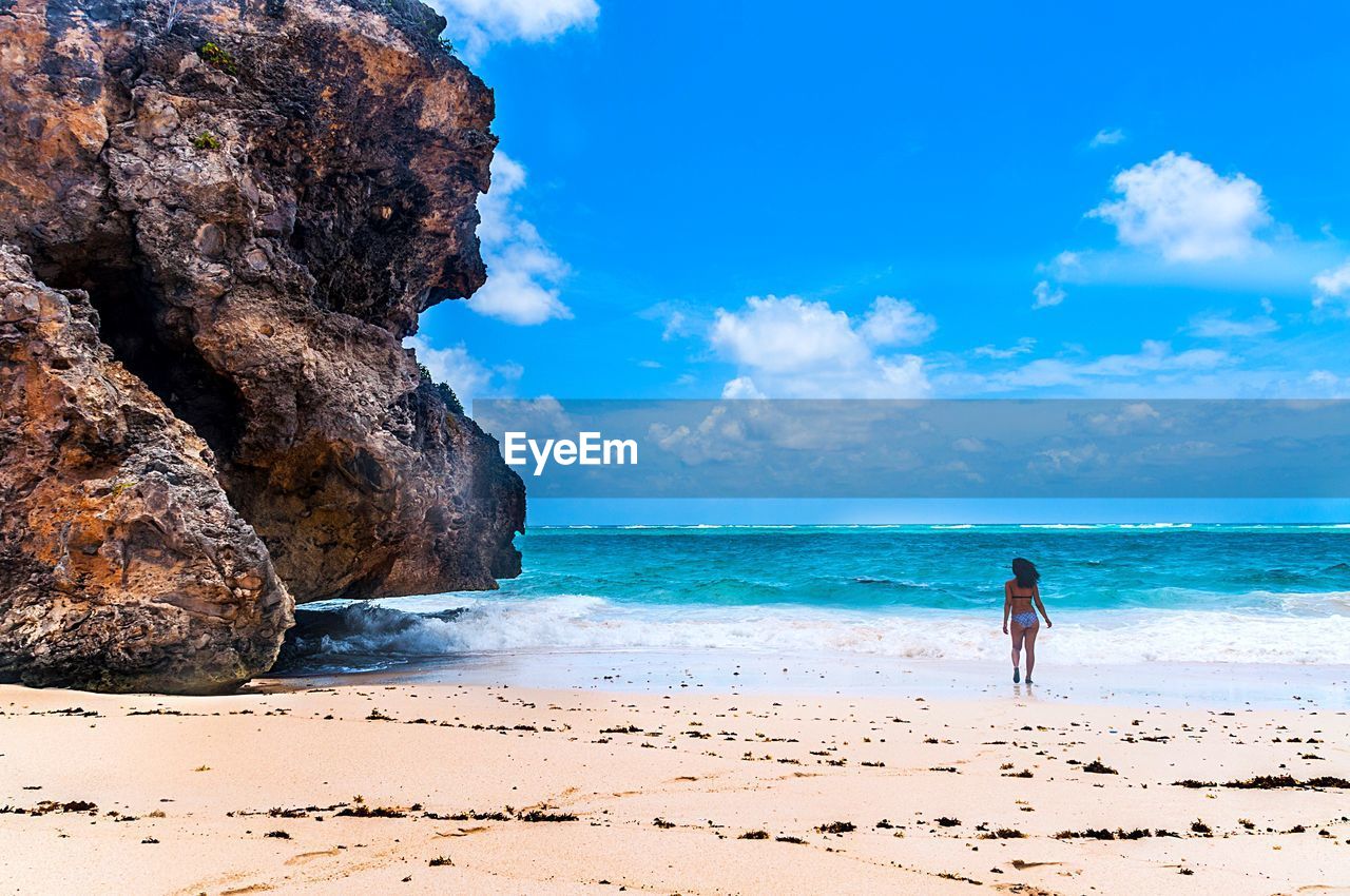 Rear view of woman walking at beach against sky