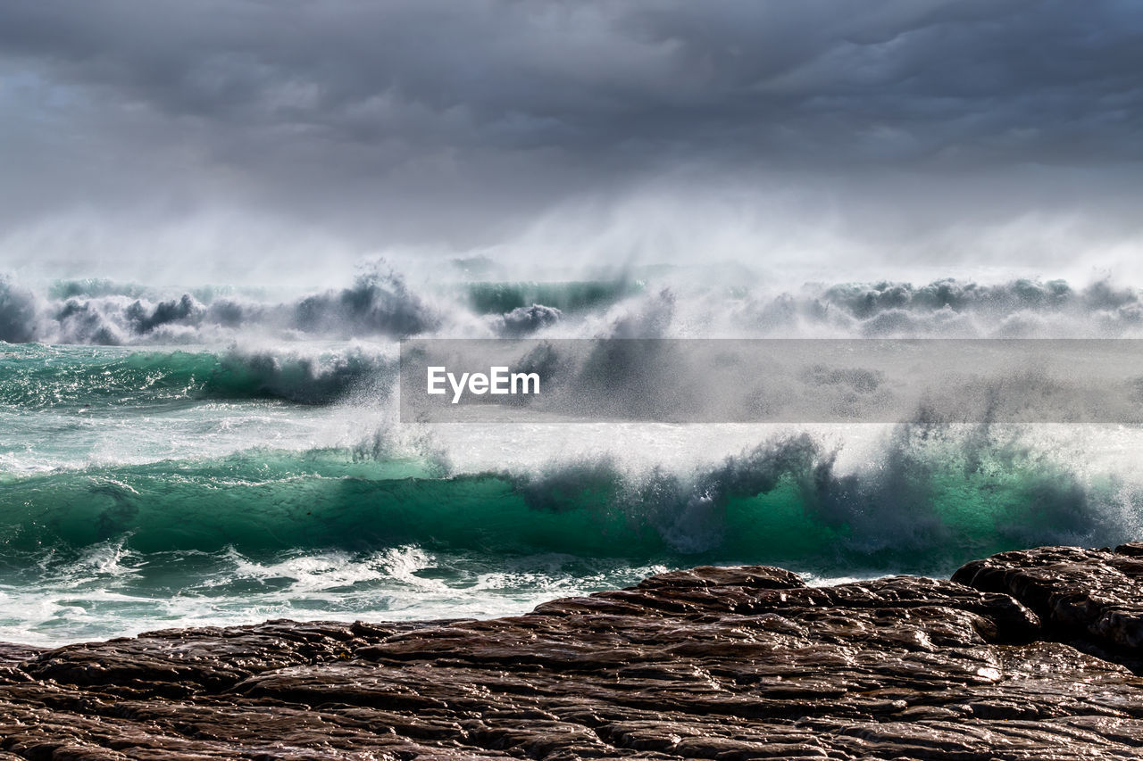 SCENIC VIEW OF WAVES BREAKING AGAINST ROCKS