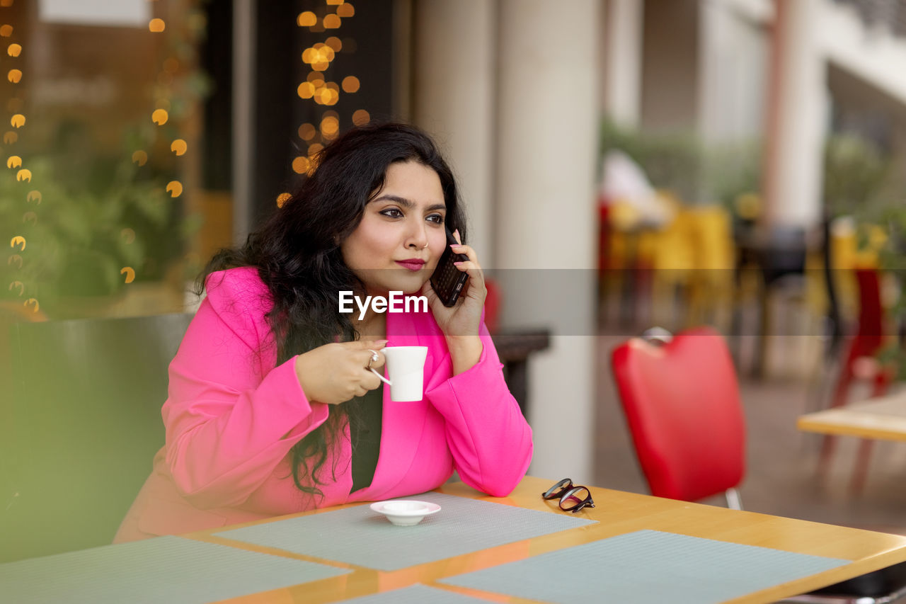 A smiling indian businesswoman is talking on her mobile phone and drinking coffee.