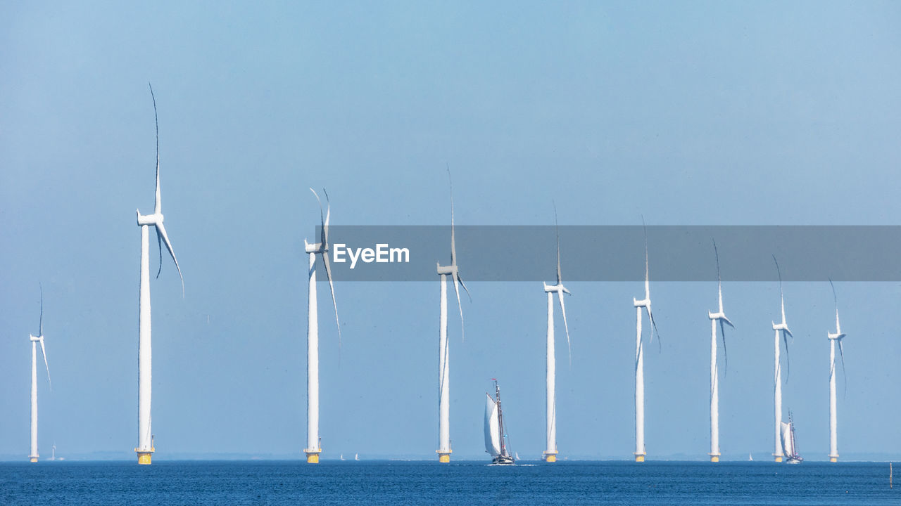 Wind turbines in sea against clear sky