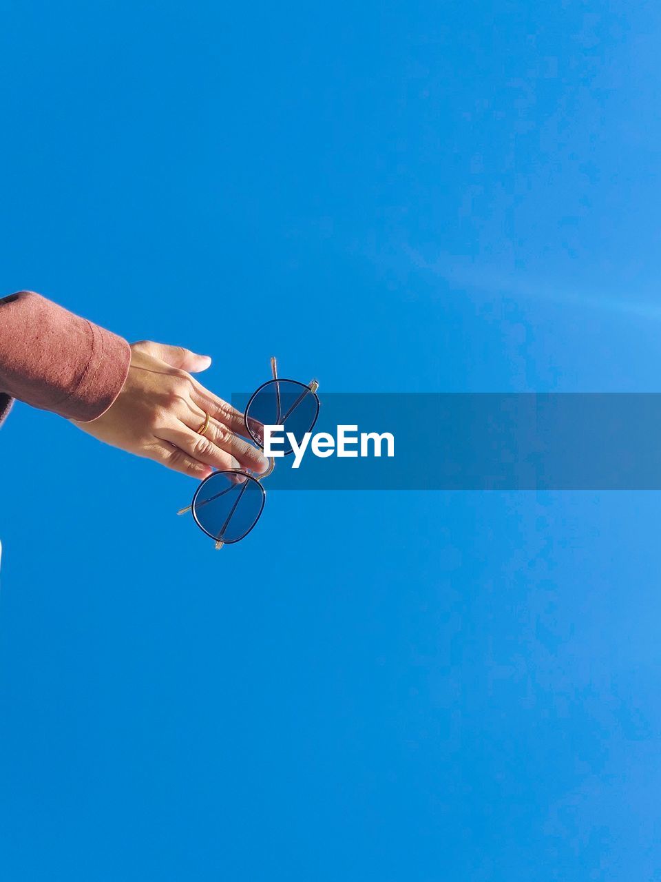 Low angle view of man holding plant against clear blue sky
