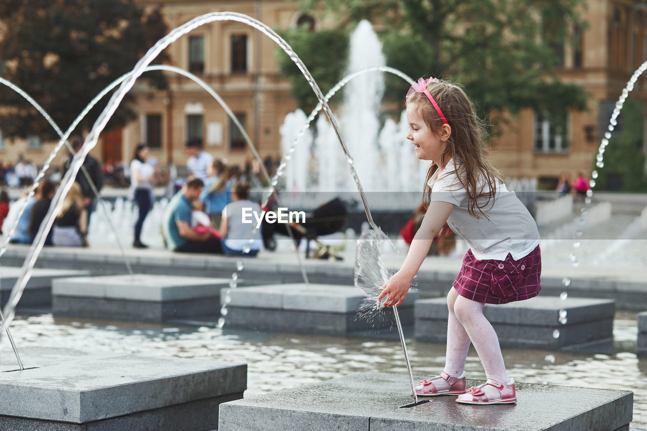 Full length of girl standing by fountain in city