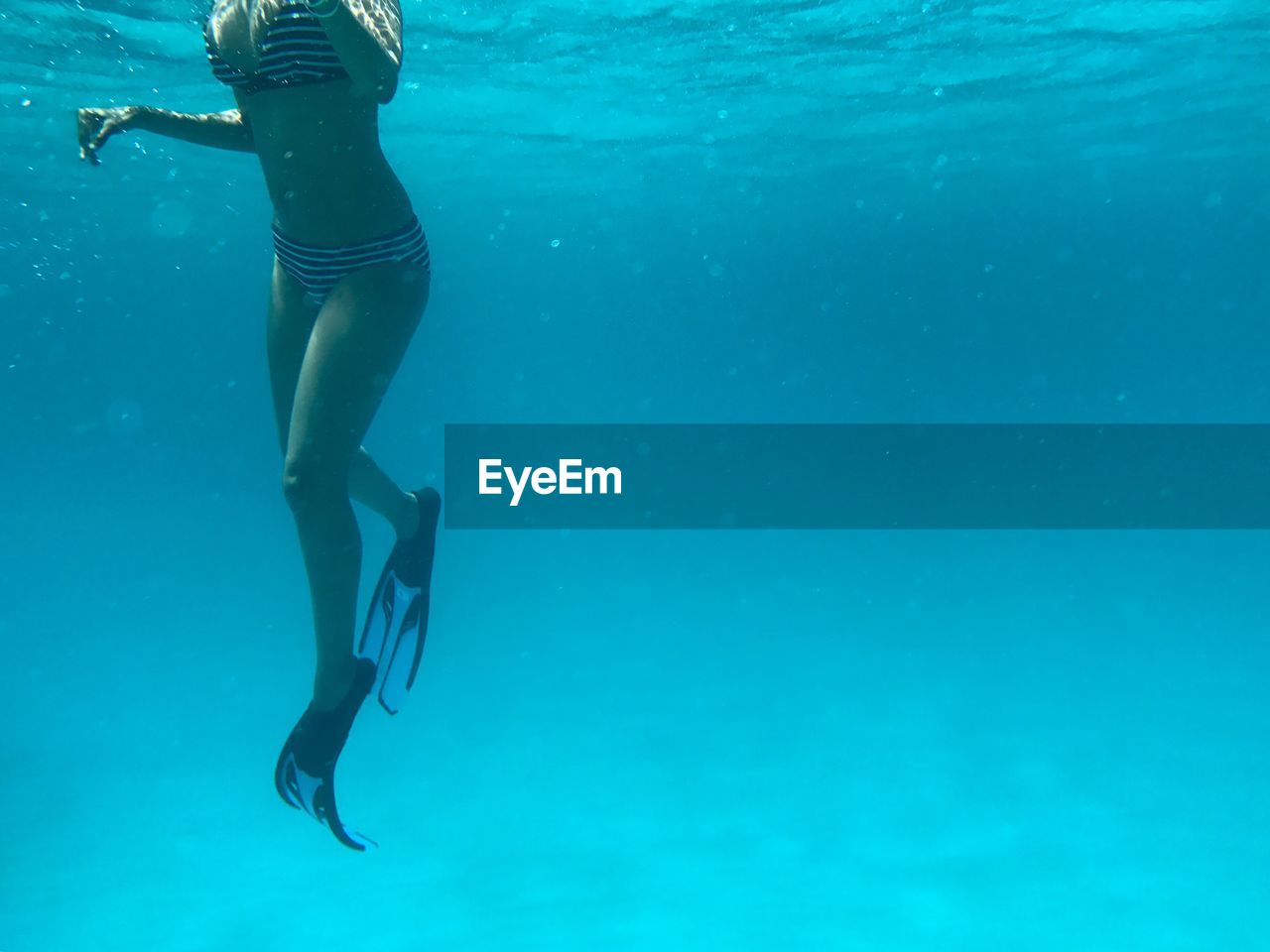 LOW SECTION OF YOUNG WOMAN SWIMMING UNDERWATER