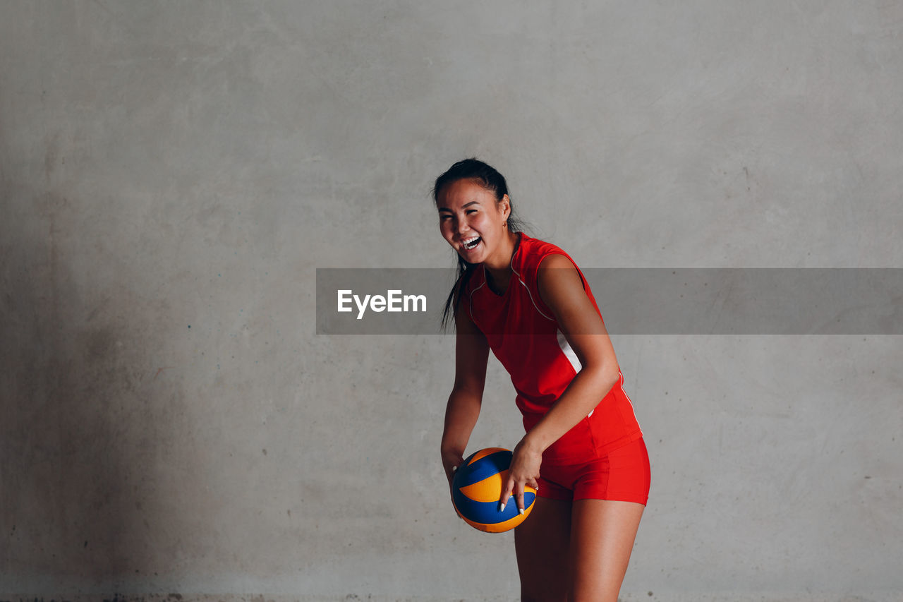 Portrait of smiling young woman standing against wall