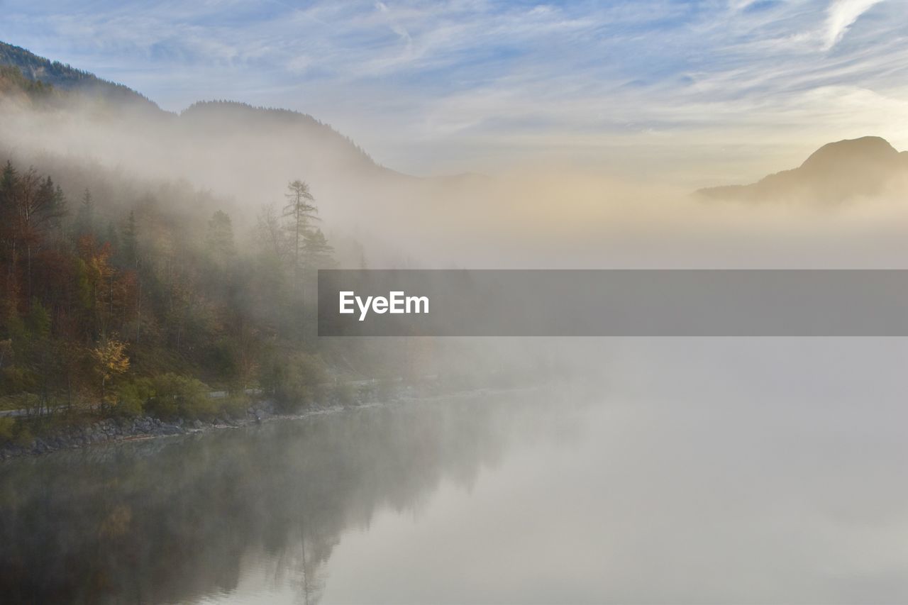 Scenic view of lake with fog against sky during sunset