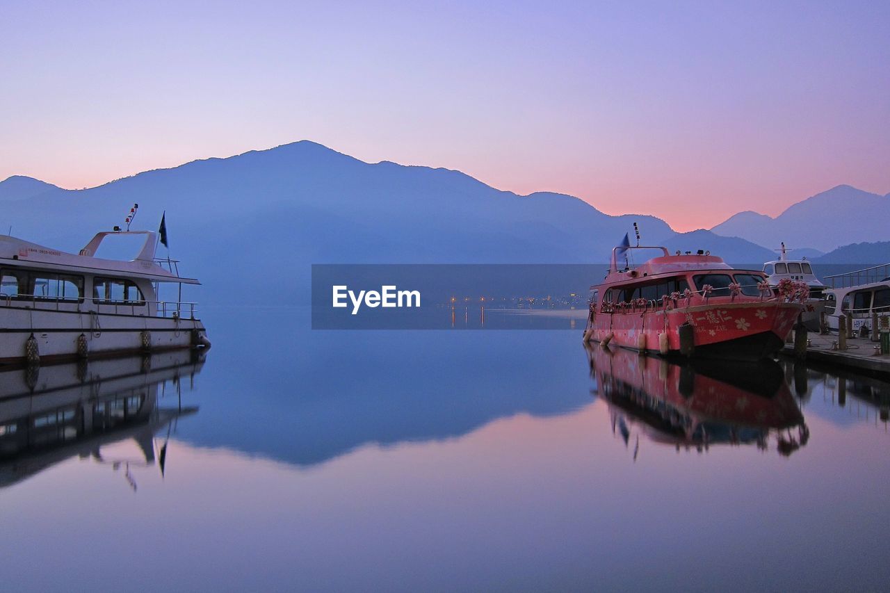 Boats moored in lake against mountains at dusk
